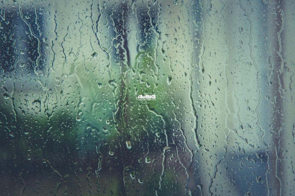 Close-up of raindrops on a window with a blurred natural backdrop, evoking a rainy day mood.